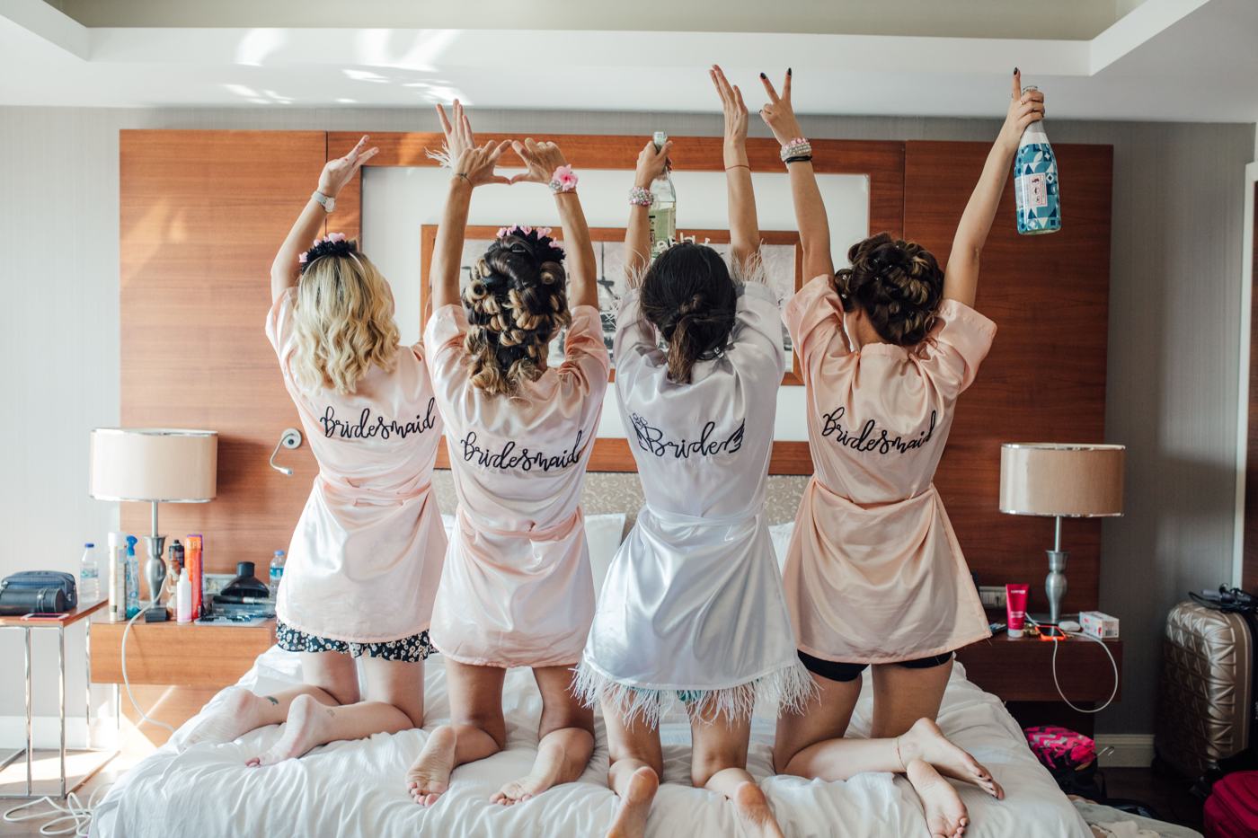 Four friends in matching robes celebrate on a hotel bed