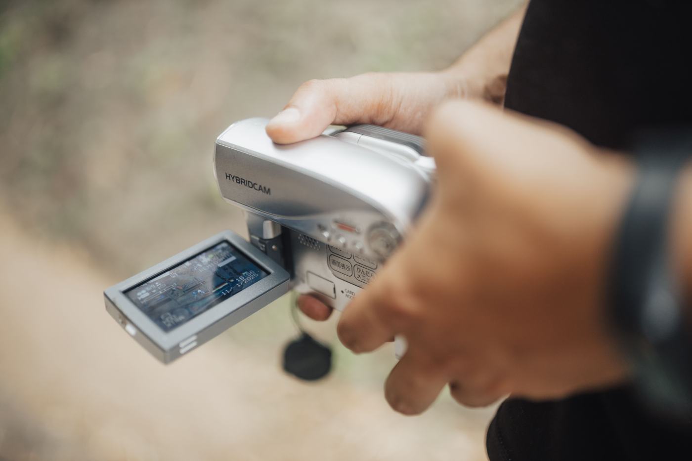 Hands hold a small camcorder with its screen flipped open